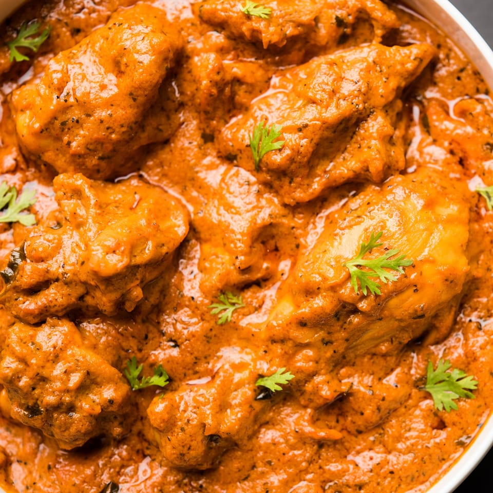 Close-up of Grains Indian Cuisine's butter chicken, featuring tender chicken pieces in a rich, orange sauce.